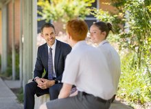 A teacher interacting with two students in an outdoor setting.