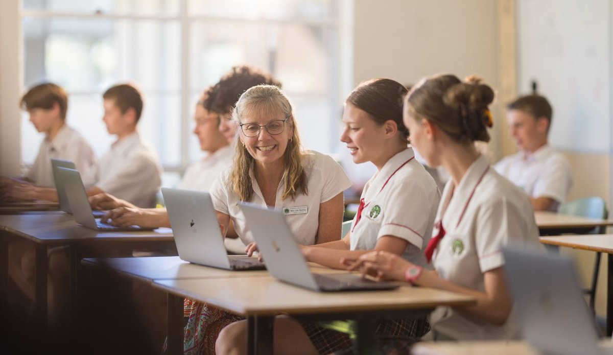A teacher interacting with students using their laptops in a classroom.