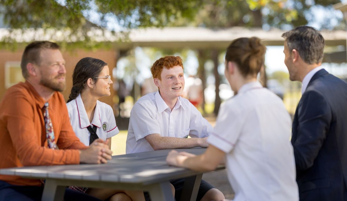 Students and teachers interacting at an outdoor table.