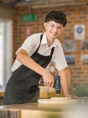 a student using a drill in the woodwork classroom.