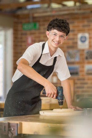 a student using a drill in the woodwork classroom.